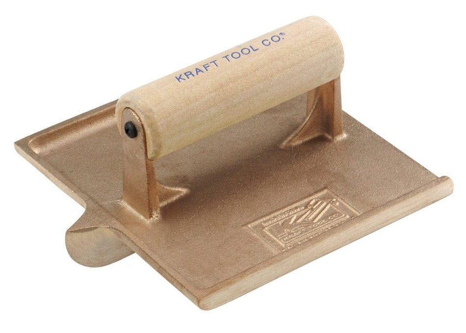 Studio view of the Kraft Tool bronze concrete hand groover featuring a 6 inch by 6 inch cast bronze square body with a central grooving bit and a smooth wood handle stamped with the brand logo.