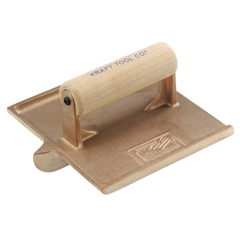 Studio view of the Kraft Tool bronze concrete hand groover featuring a 6 inch by 6 inch cast bronze square body with a central grooving bit and a smooth wood handle stamped with the brand logo.