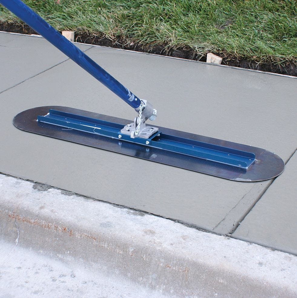 High angle view of the blue steel bull float blade smoothing a section of wet concrete flatwork next to a curb.