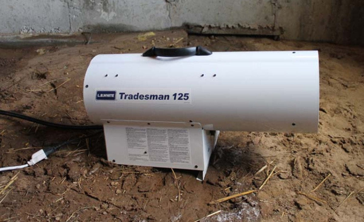 A Tradesman 125 heater sitting on dirt ground at a construction site, plugged in and connected to a gas line, ready for operation.