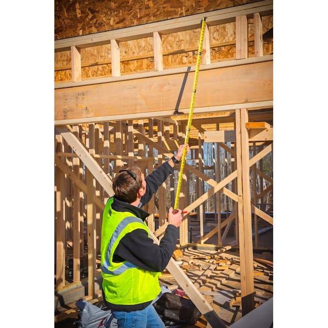 A worker in a safety vest demonstrates the 15-foot standout of the Lufkin Shockforce tape measure by extending the blade vertically to measure an overhead beam.