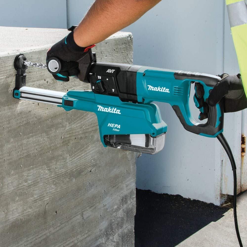 Worker in safety gear using Makita HR2661 rotary hammer drill horizontally on a concrete wall. HEPA dust extractor is actively capturing debris during operation
