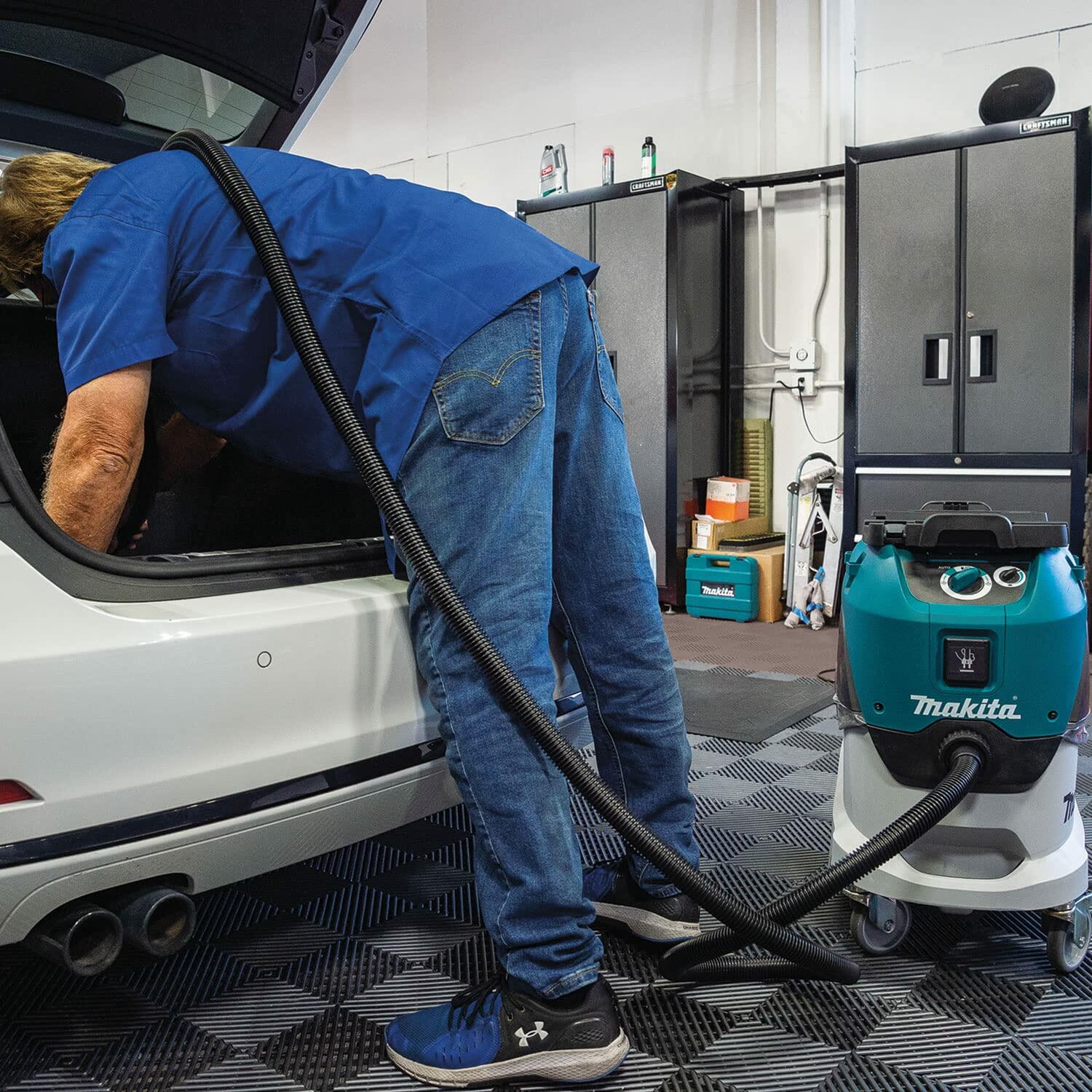 Person using Makita VC4210L vacuum to clean the trunk of a white car in a workshop, highlighting the vacuum’s mobility and automotive detailing use.