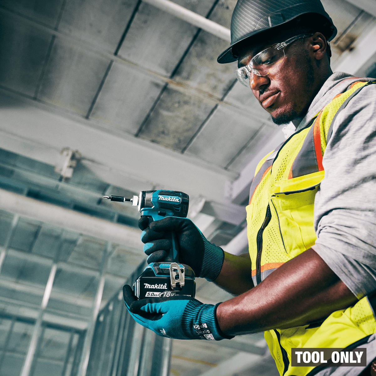 Construction worker holding a compact Makita XDT20 18V LXT brushless impact driver on a commercial jobsite.