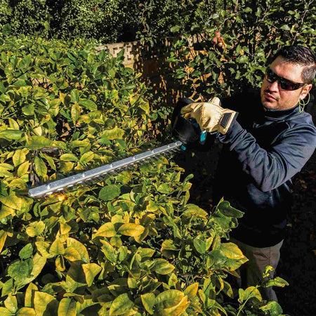 Perspective shot of a worker utilizing the high-speed 4,000 SPM Makita brushless hedge trimmer to maintain ornamental landscaping, highlighting the tool's effectiveness on thick branches.