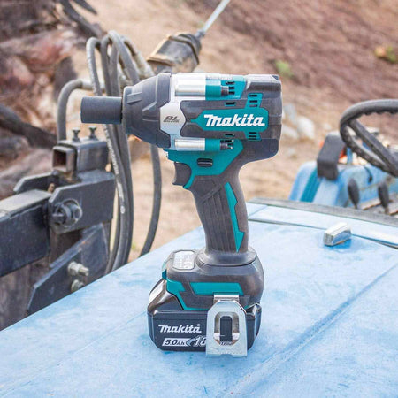The Makita XWT18T brushless impact wrench with a 5.0Ah battery attached, shown standing on a blue metal surface in an outdoor work environment.