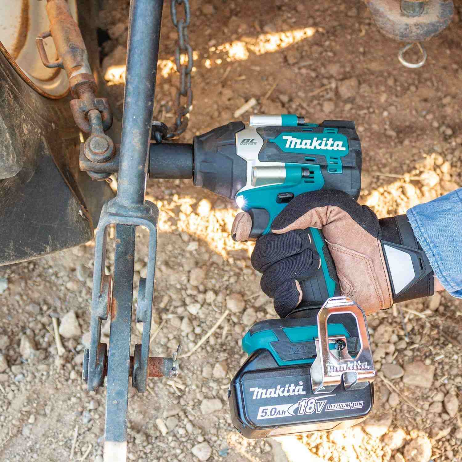 A gloved hand uses the Makita XWT18T impact wrench to tighten or loosen a large bolt on a rusty piece of heavy farm equipment.