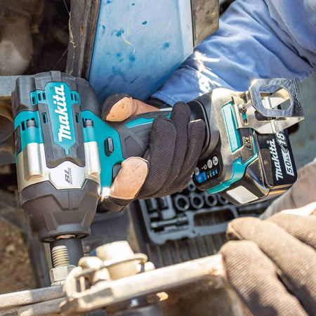 A gloved hand holds the Makita XWT18T impact wrench, positioned to tighten or loosen a large bolt on a piece of heavy equipment.