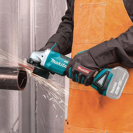 A person wearing a leather apron and gloves uses the Makita XAG11Z angle grinder to cut a metal pipe, creating a stream of sparks.