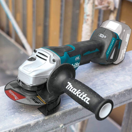 The Makita XAG11Z angle grinder with a battery and side handle attached, resting on a metal beam at a construction site.