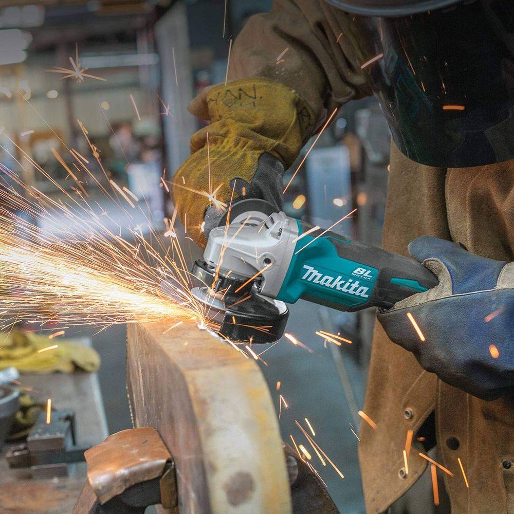 A person in a welding jacket and gloves uses the Makita XAG11Z angle grinder, sending a large shower of sparks from a thick piece of metal.