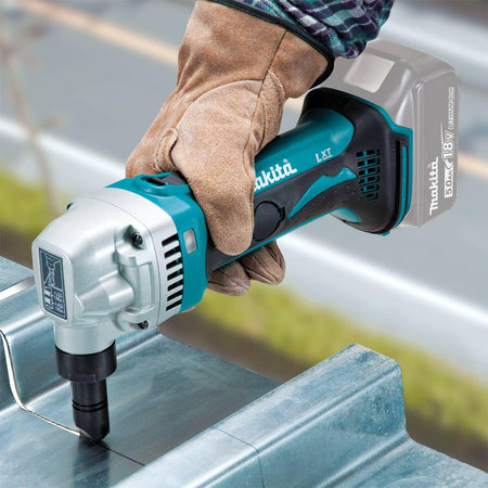 A gloved hand using the Makita 18V LXT nibbler to cut a straight line through a piece of corrugated metal roofing.