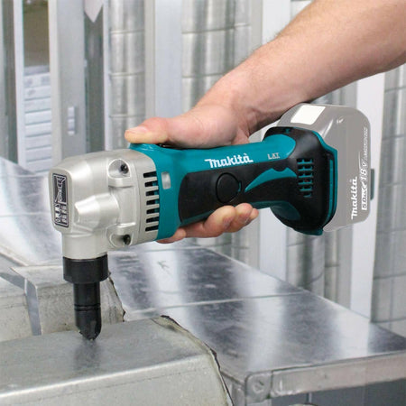A hand holding the Makita 18V LXT nibbler, making a cut in a piece of metal ductwork in a workshop.