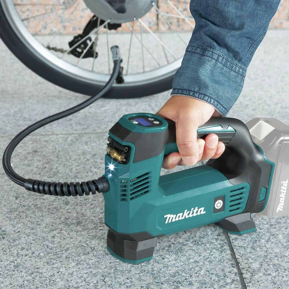 Person using Makita cordless inflator to fill a bicycle tire; device held in hand with hose connected to valve and LED light illuminated during operation.