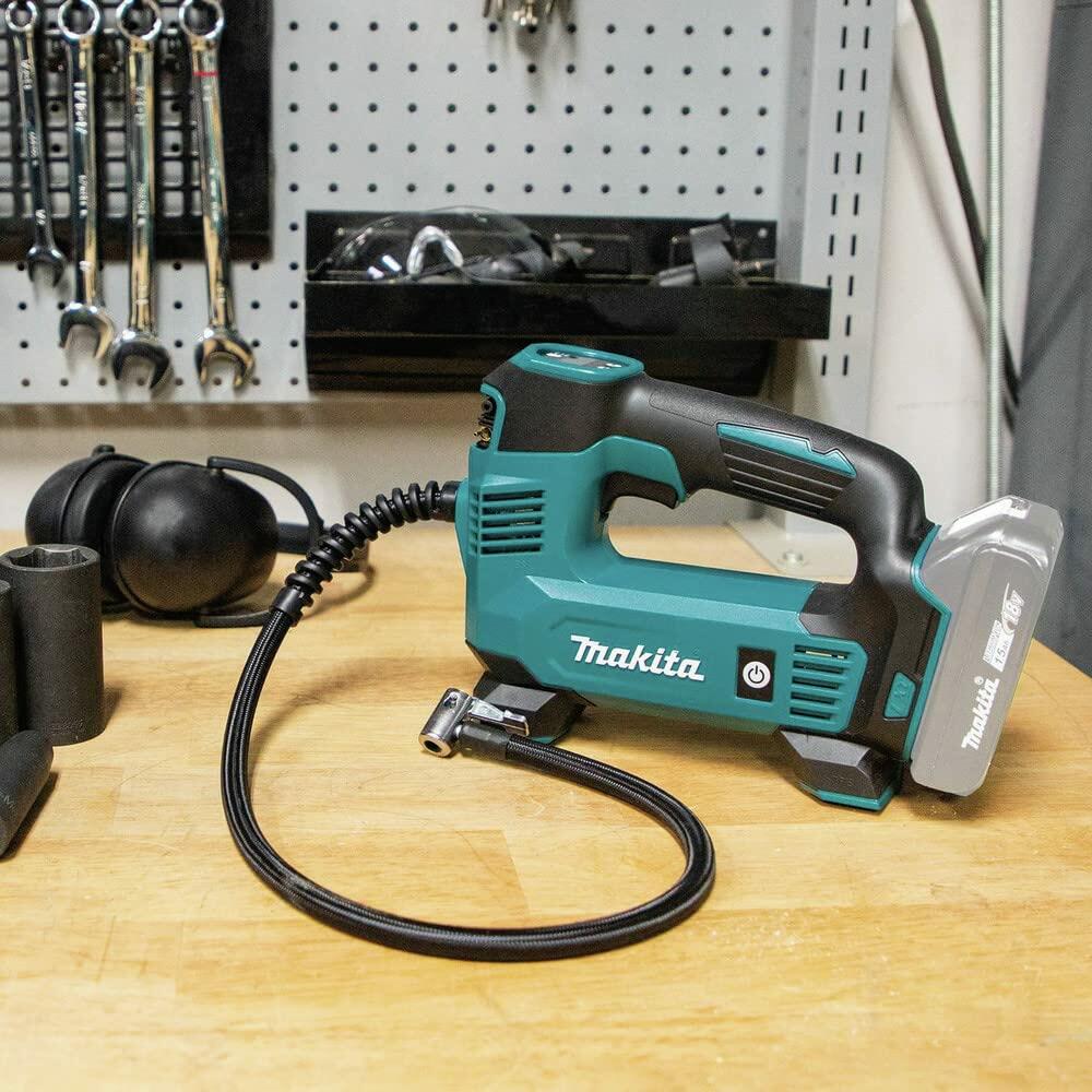 Makita cordless inflator placed on a workshop bench with hose and nozzle visible; surrounded by tools, accessories, and pegboard in background.