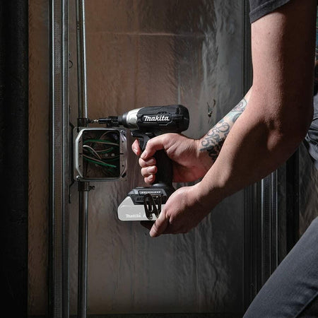 A worker using the Makita impact driver to install a metal electrical junction box onto a steel stud.