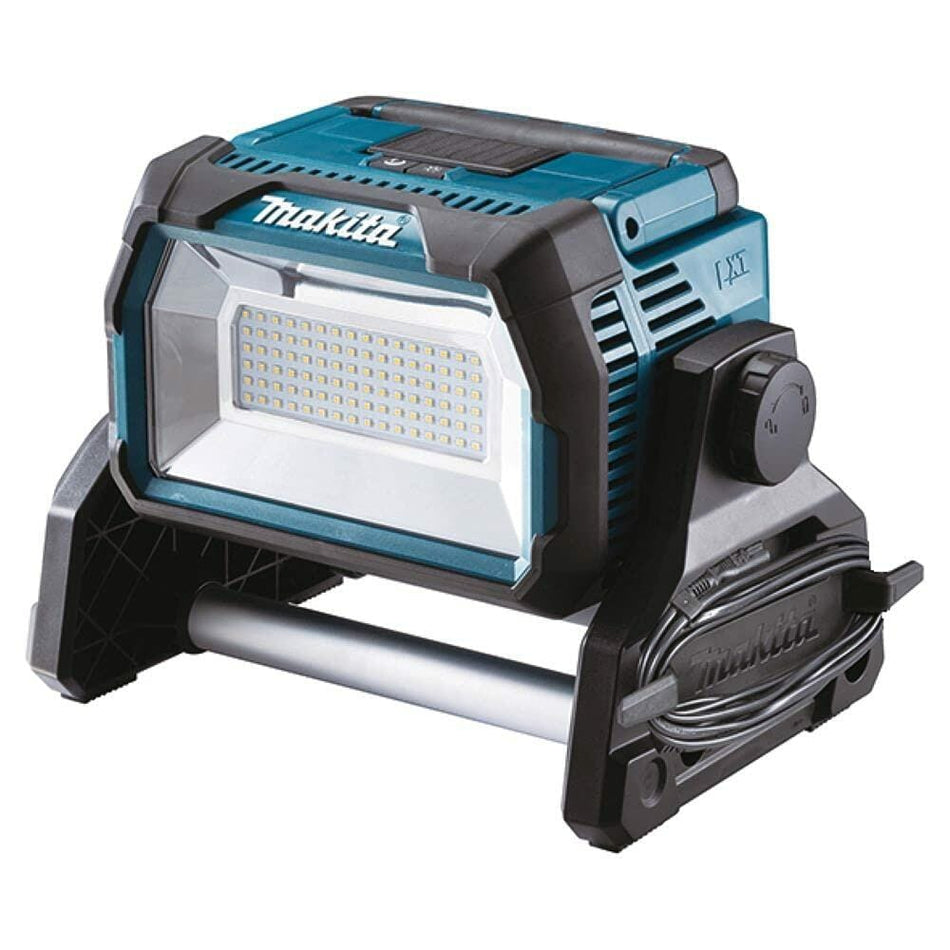 Makita LED work light with rectangular panel, top handle, and metal support bar; cord wrap and control knob visible on rugged base.