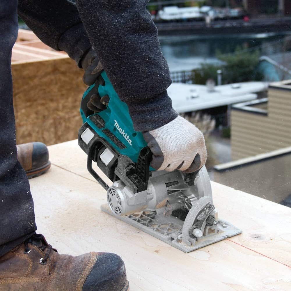Action shot of a professional contractor in safety gloves using the Makita 36V rear handle circular saw to perform a precise cross-cut on a sheet of plywood at a residential jobsite.