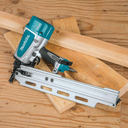 The Makita AN924 framing nailer resting on a stack of lumber and plywood, ready for use.