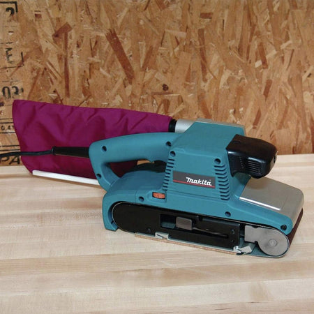 Blue Makita belt sander on a wooden surface with a purple sanding block in the background.