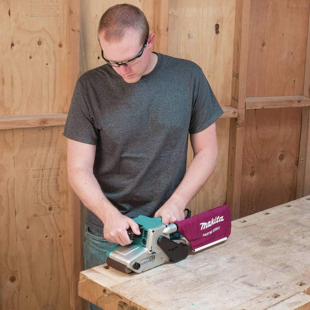 Person using a Makita belt sander on a wooden surface.