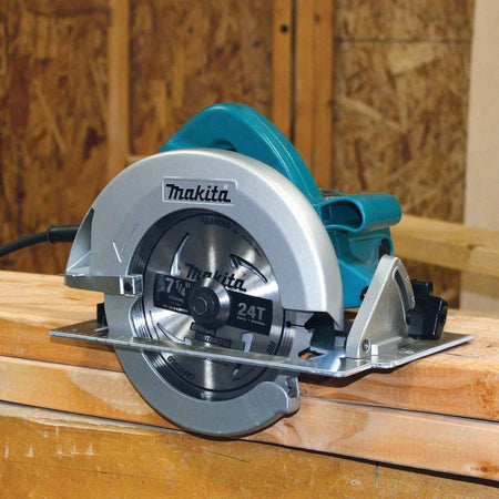 The Makita 5007F 7-1/4 inch circular saw is shown resting on a 2x4 wooden stud at a construction site, providing a clear view of the 24-tooth Makita framing blade.