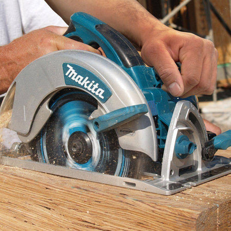 Action shot of a worker's hands guiding the Makita 7-1/4 inch circular saw through a dense piece of dimensional lumber, illustrating professional framing and cutting.