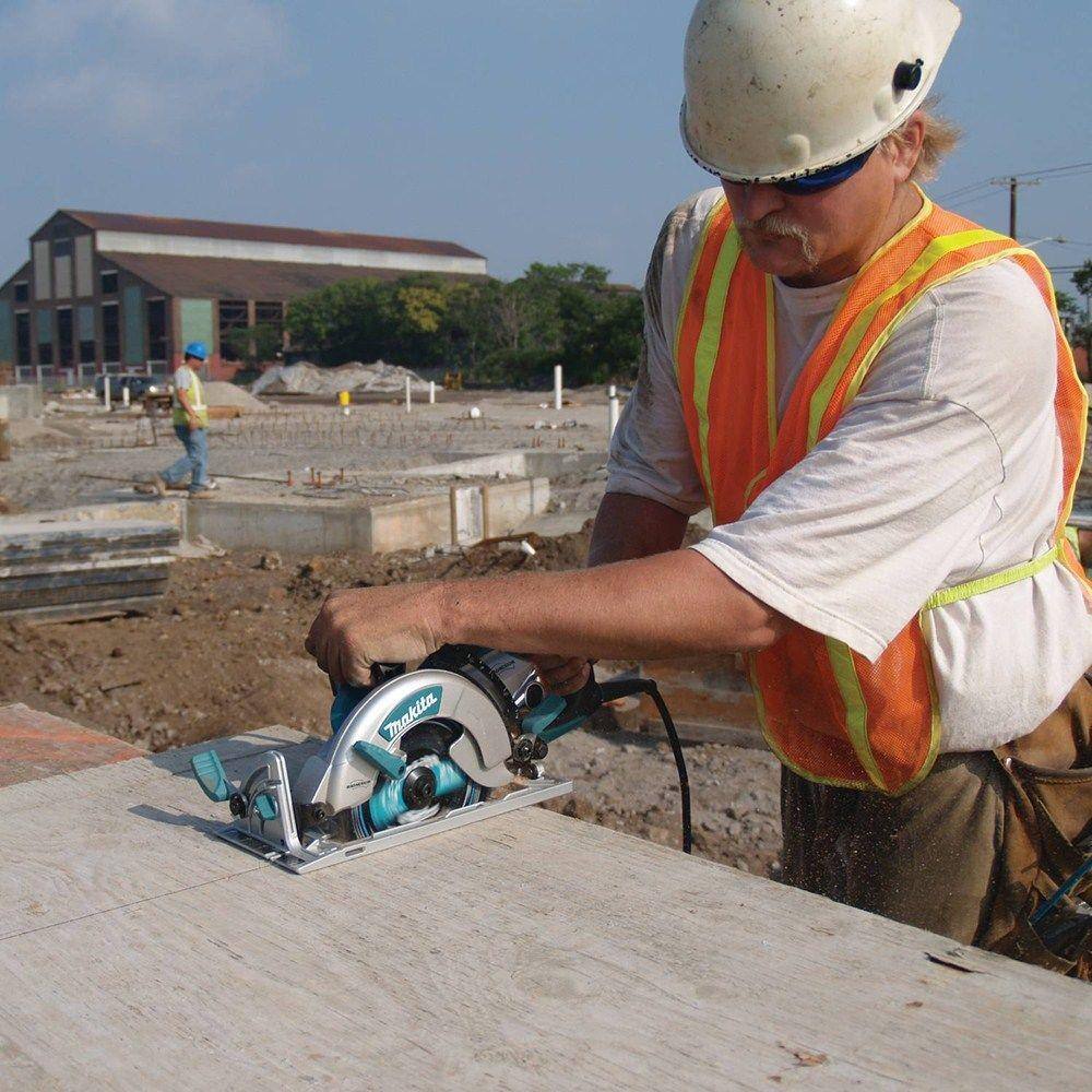 Action shot of a professional installer using the Makita 7-1/4 inch hypoid saw to cut through thick dimensional lumber, highlighting the superior torque and balance of the magnesium design.