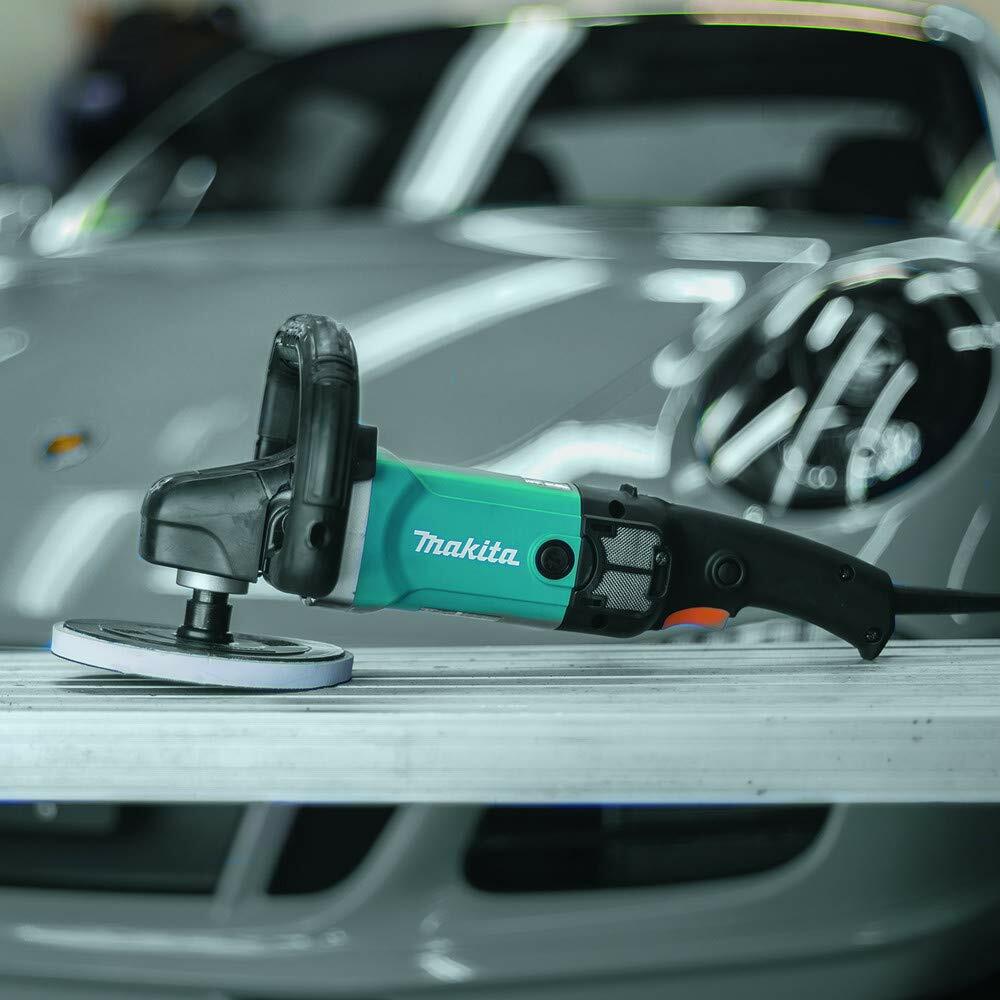 The Makita 9237CX3 polisher resting on a workbench with a luxury silver sports car blurred in the background of a detailing garage.