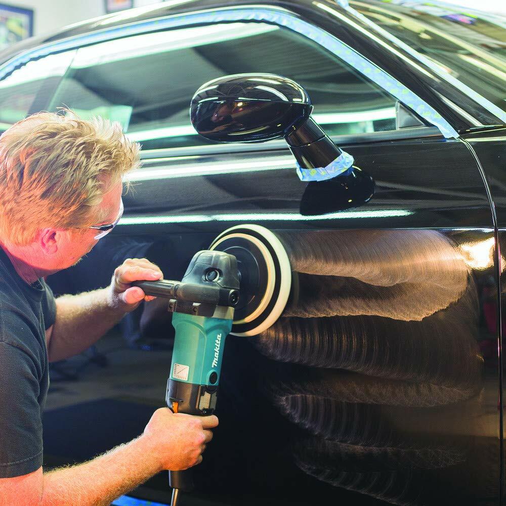 A professional detailer using the Makita polisher with a wool bonnet to polish the side of a black car, showing the swirl-free finish being achieved.