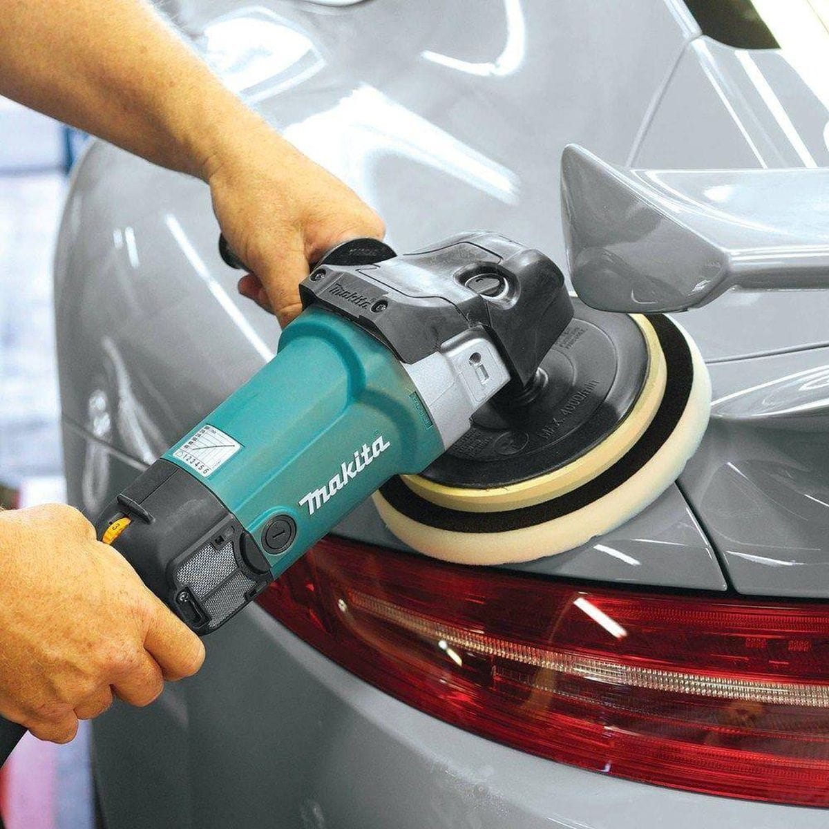 A professional detailer using the Makita 9237C 7-inch polisher with a wool bonnet to restore the high-gloss clear coat finish on the hood of a vintage automobile.