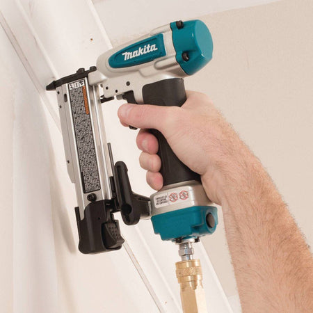 A professional carpenter using the Makita AF353 pneumatic 23 gauge pin nailer to securely install white crown moulding trim near a ceiling.