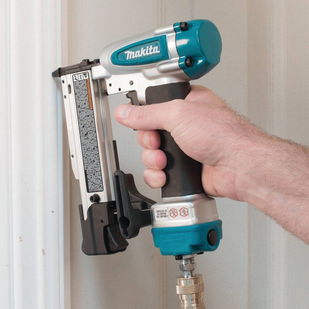 Action shot of a woodworker driving a fastener into white door casing trim with the Makita AF353 air powered 23 gauge pin nailer.