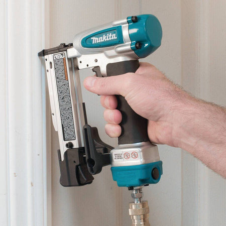 Action shot of a woodworker driving a fastener into white door casing trim with the Makita AF353 air powered 23 gauge pin nailer.