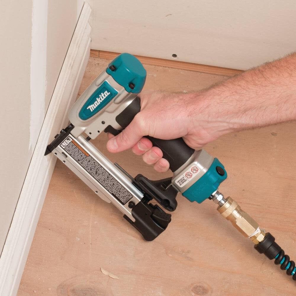 A user operating the Makita AF353 pneumatic pin nailer to easily secure wood baseboard trim to a wall during a finish carpentry project.