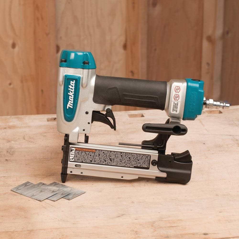 The Makita AF353 23 gauge pneumatic pin nailer resting on a wooden workbench alongside strips of headless pin fasteners for woodworking and cabinet building.