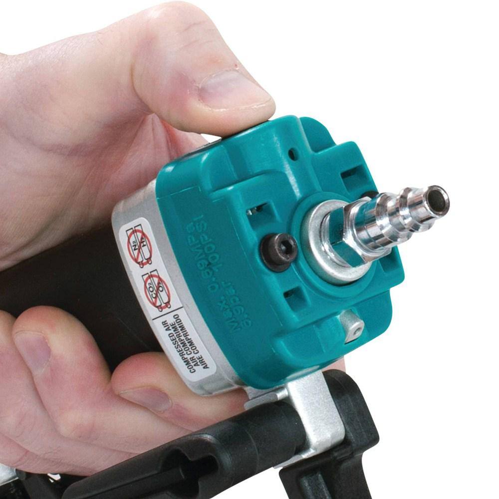 Close-up of a thumb pressing the built-in air duster button near the rear exhaust port of the Makita AF353 pneumatic pin nailer to easily clear dust from a workspace.