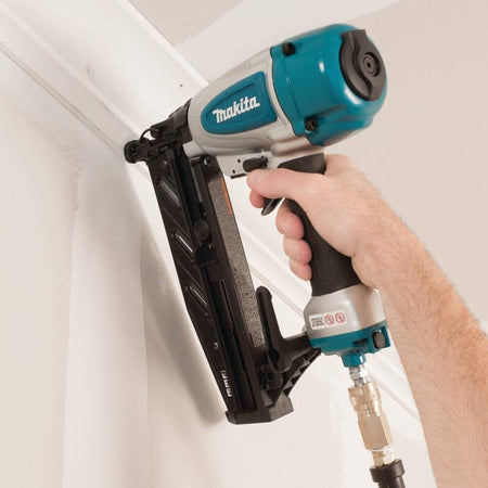 A professional carpenter using the Makita AF601 pneumatic 16 gauge straight finish nailer to quickly and securely install white baseboard trim along a wall.