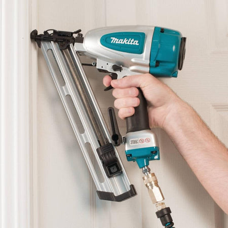 A professional carpenter using the Makita AF635 pneumatic 15 gauge angled finish nailer to securely install white crown molding trim during a woodworking project.