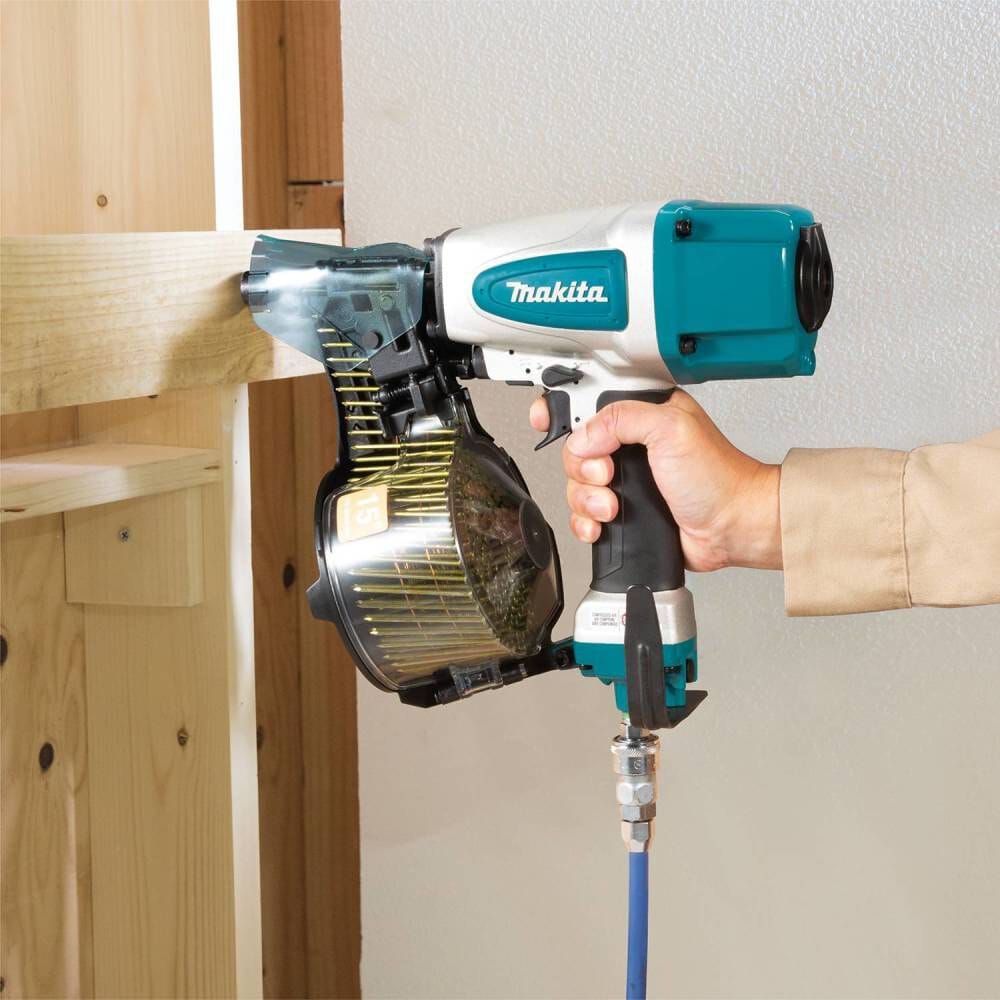 A professional contractor efficiently operating the Makita AN613 2-1/2 inch pneumatic siding coil nailer to securely fasten a wooden board during a construction project.