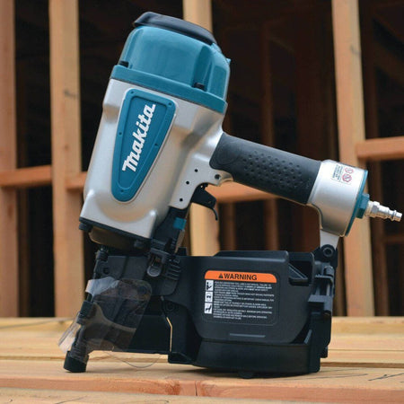 Side profile of the Makita AN902 air powered coil framing nailer resting on a wooden construction surface with a framing project visible in the background.
