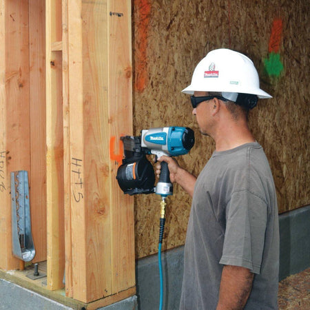 Detailed shot of a contractor accurately positioning the Makita AN902 pneumatic coil nailer against a vertical wooden stud for high-production framing.