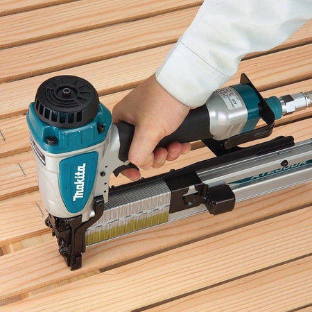 User operating a Makita pneumatic nailer over wooden planks with collated nails loaded, illustrating professional‑grade fastening similar to the AT2550A wide crown stapler workflow.