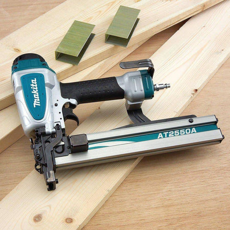 Makita AT2550A Pneumatic 16 Gauge Wide Crown Stapler placed on wood planks with staple packs nearby, highlighting top‑loading magazine and jobsite‑ready construction.