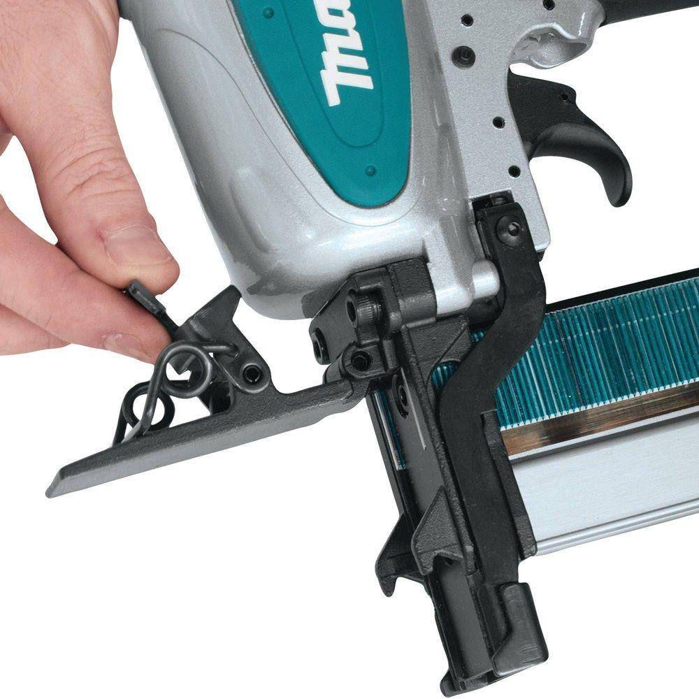 Close‑up of a user adjusting the front mechanism on a Makita AT2550A Pneumatic Wide Crown Stapler with collated staples loaded, demonstrating tool‑less depth adjustment and safety operation.