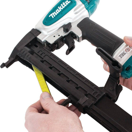A woodworker loading a strip of 18 gauge 1/4 inch narrow crown staples into the high-efficiency bottom-loading magazine of the Makita AT638A pneumatic stapler.