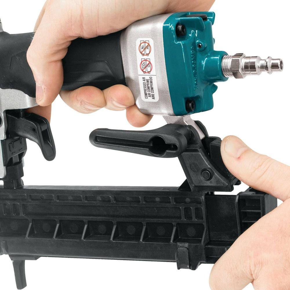 Close-up of a hand gripping the Makita AT638A pneumatic stapler, highlighting the reversible belt hook and the 1/4 inch NPT air inlet fitting.
