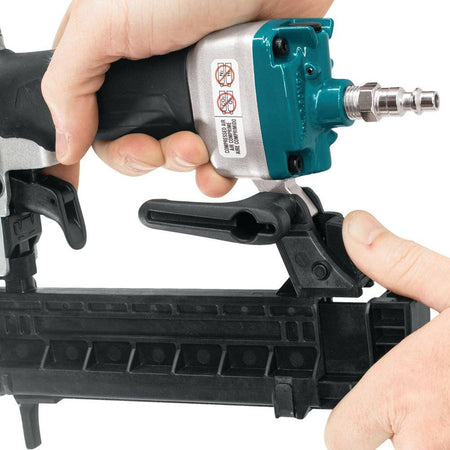 Close-up of a hand gripping the Makita AT638A pneumatic stapler, highlighting the reversible belt hook and the 1/4 inch NPT air inlet fitting.