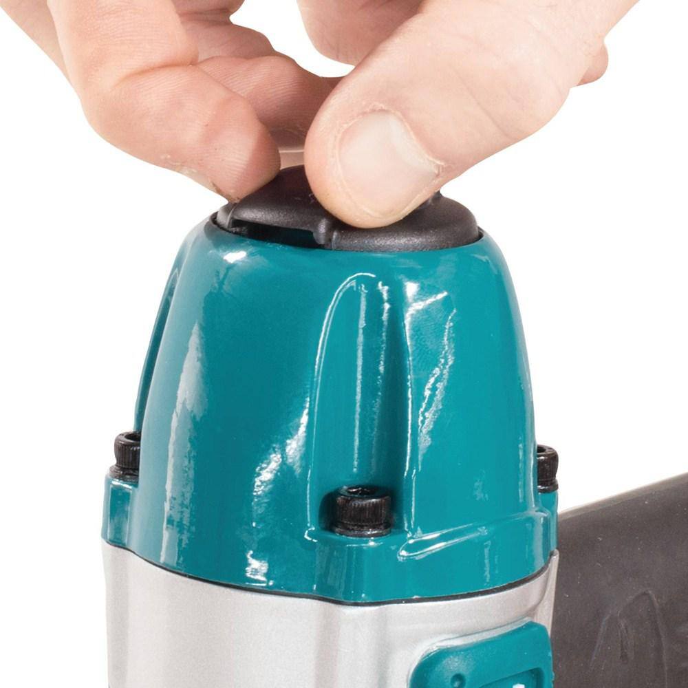 Close-up of a user pressing the built-in air duster button on the top of the Makita AT638A pneumatic stapler to clear sawdust from a woodworking surface.