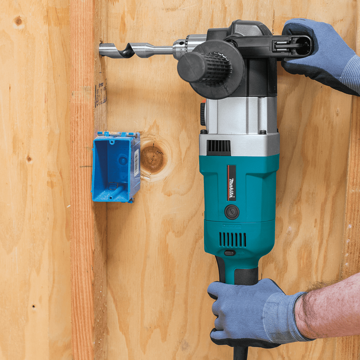 Professional contractor drilling a hole with an auger bit through a wooden wall stud adjacent to an electrical box.